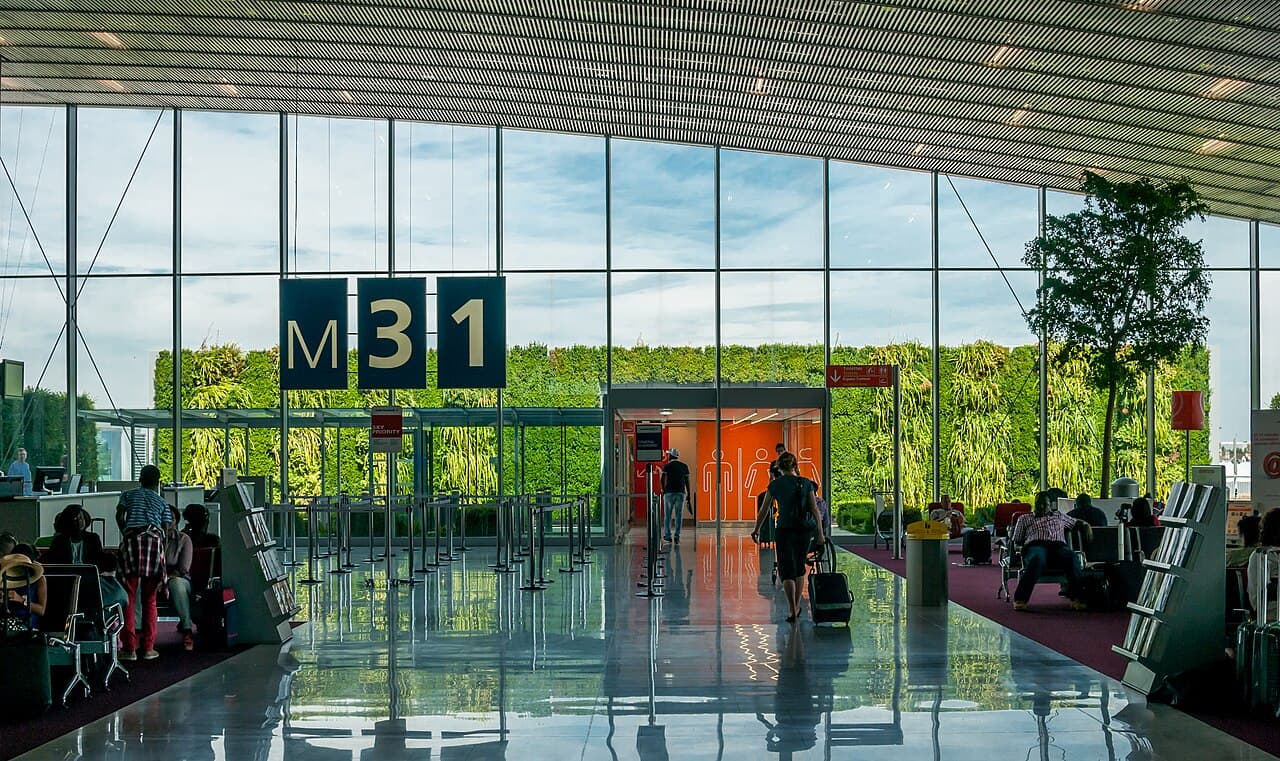 A traveller walking with luggage through a bright terminal hall at Paris Charles de Gaulle Airport